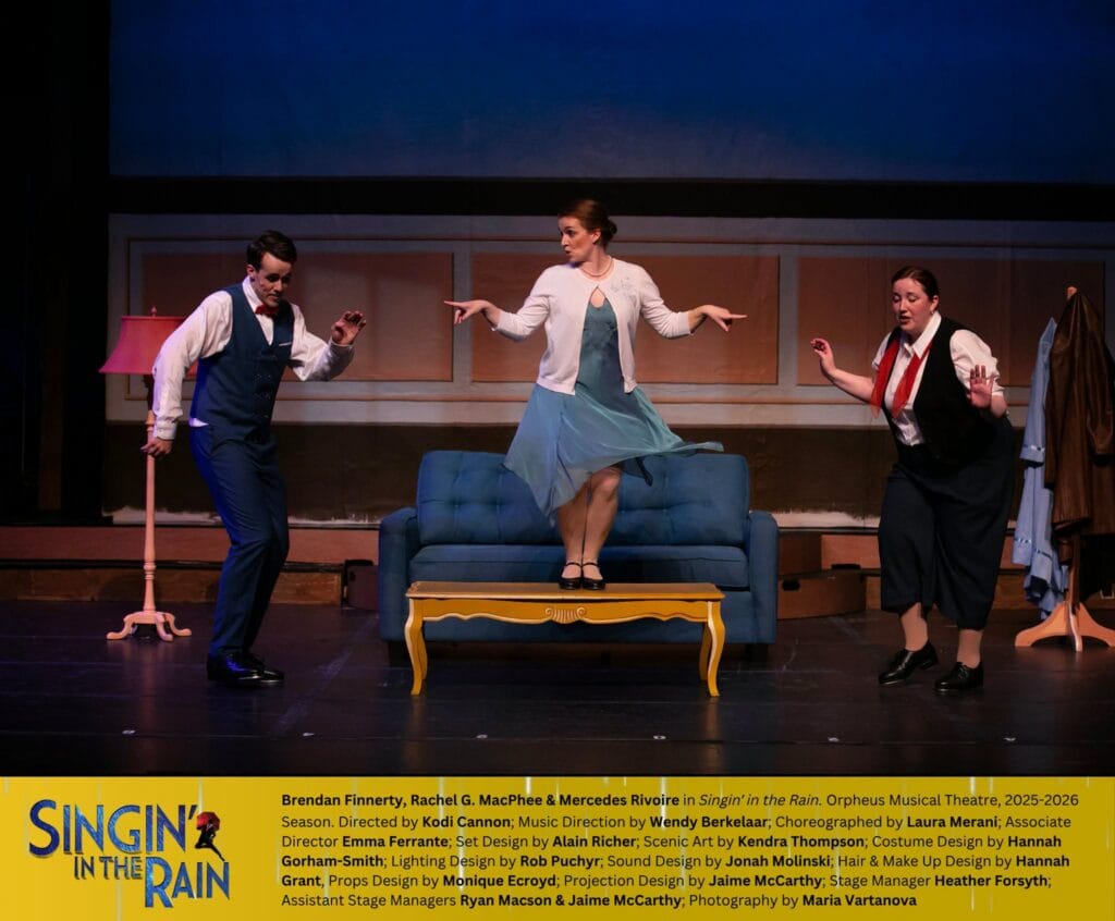 The three main characters of Singin' in the Rain are tap dancing. Two are wearing black and white, dancing on the floor. The third dancer dances on a coffee table in front of a sofa. She wears a blue dress with a white cardigan. At the bottom of the photo, in a yellow rectangle, is the "Singin' in the Rain" title and credits to the cast and crew.